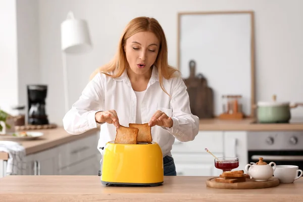Mature woman making tasty toasts in kitchen