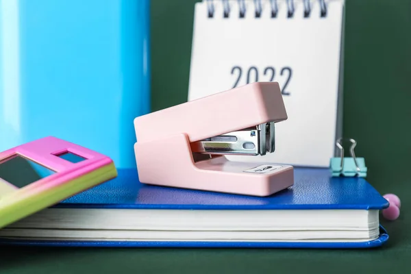 Stapler with book and calendar on green background, closeup