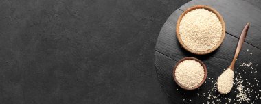 Bowls and spoon with sesame seeds on dark background with space for text