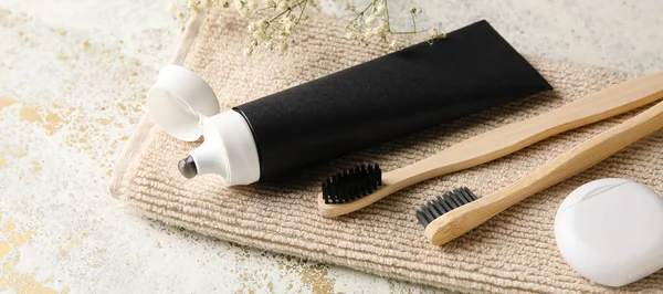Activated charcoal toothpaste, brushes, floss and towel on table