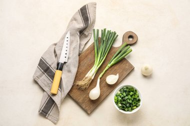 Açık arkaplanda taze yeşil soğan ve bıçaktan oluşan ahşap bir kompozisyon.