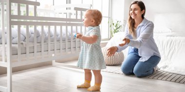Mother teaching her cute baby to walk at home