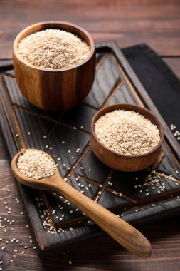 Tahta masa üzerinde kaşık ve kase dolusu susam tohumu, yakın plan.