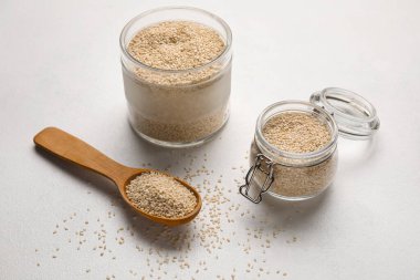 Işık arka planında kase, kavanoz ve kaşık dolusu susam tohumu