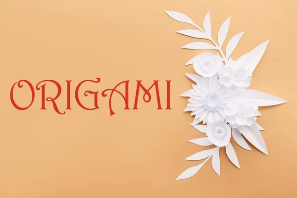 Beautiful handmade paper flowers, leaves and word ORIGAMI on beige background