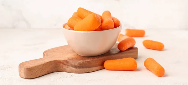 Bowl with fresh baby carrots on white table