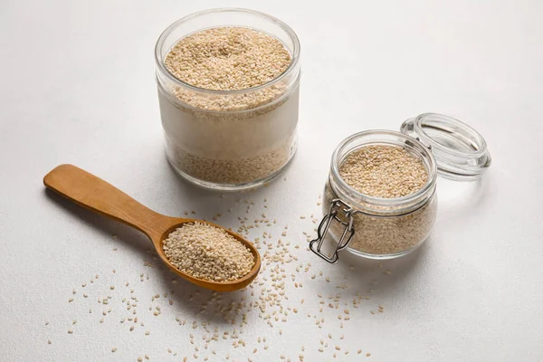 Işık arka planında kase, kavanoz ve kaşık dolusu susam tohumu