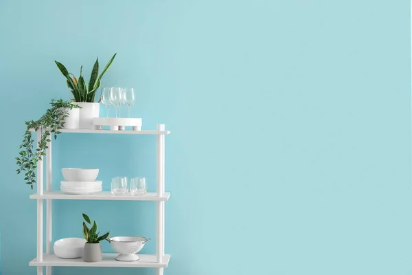 Shelving unit with houseplants and tableware near blue wall