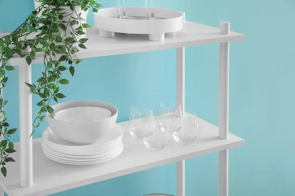 Shelving unit with houseplants and tableware near blue wall