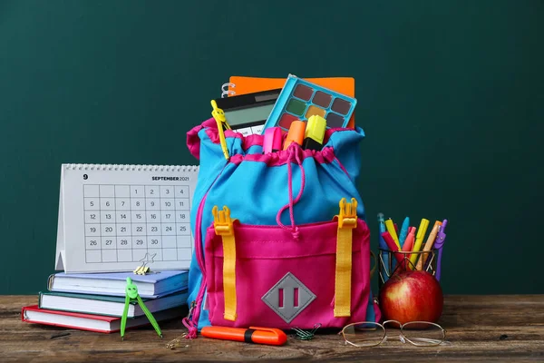 School backpack with stationery, calendar, apple and eyeglasses on table against green background