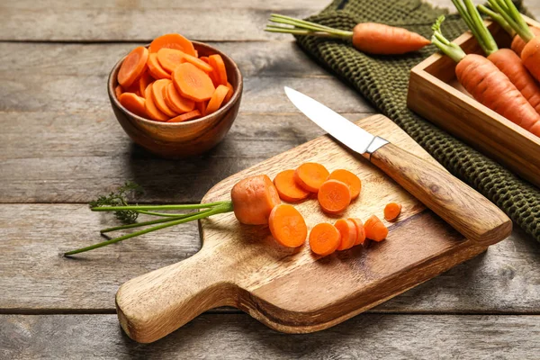 Board with cut carrot and knife on wooden table