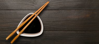 Koyu ahşap zemin üzerinde bir kase soya sosu ve yemek çubuğu, metin ve üst görünüm için yer var.