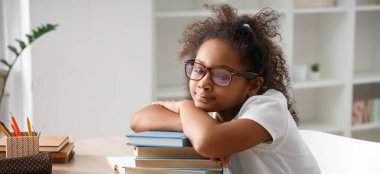 Little African-American schoolgirl with books studying at home