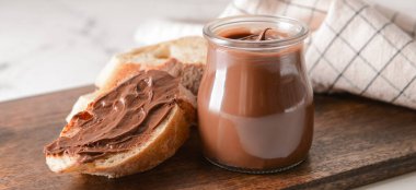 Lezzetli çikolata ezmeli kavanoz ve masada ekmek.