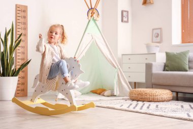 Cute little girl playing with rocking horse at home