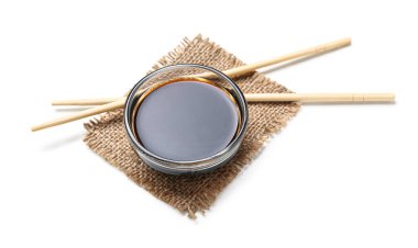 Beyaz arka planda bir kase soya sosu, yemek çubukları ve çuval bezi.