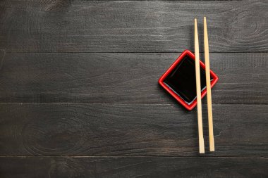 Bowl of soy sauce and chopsticks on dark wooden background