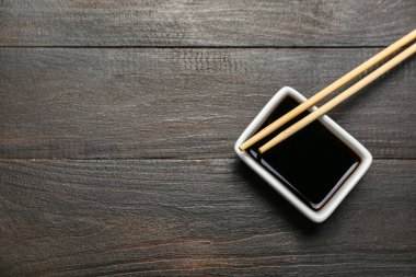 Koyu ahşap arka planda bir kase soya sosu ve yemek çubuğu.