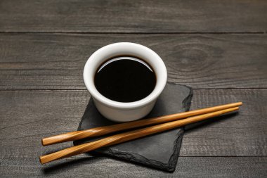 Koyu ahşap arka planda soya sosu ve çubuklarla dolu bir tahta.