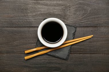 Koyu ahşap arka planda soya sosu ve çubuklarla dolu bir tahta.