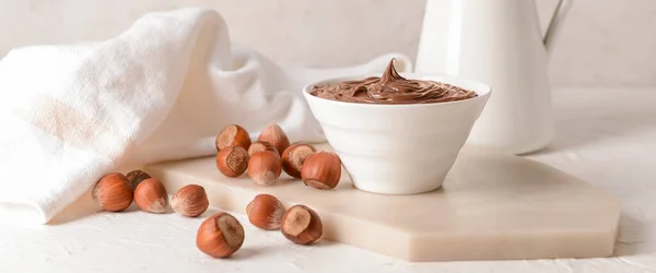 Bowl with tasty chocolate paste and hazelnuts on light table