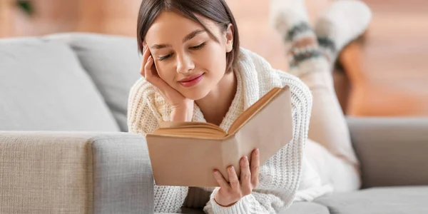 Beautiful Young Woman Reading Book While Lying Sofa Home — Φωτογραφία Αρχείου