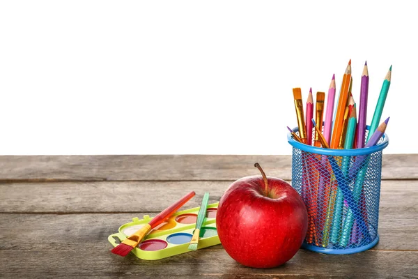 Pencil cup with brushes, paints and apple on table against white background