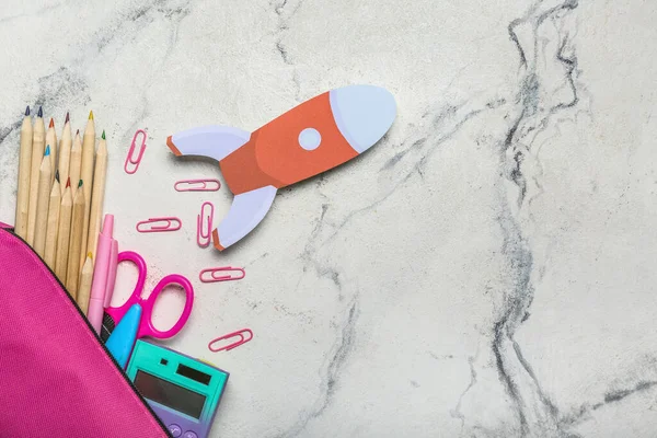 Okul kırtasiyesi ve arka planda kağıt roketli kalem kutusu