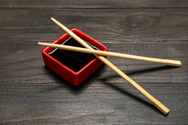 Bowl of soy sauce and chopsticks on dark wooden background