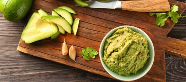 Tahta tahtada leziz guacamole ve dilimlenmiş avokado ile kase, üst manzara.