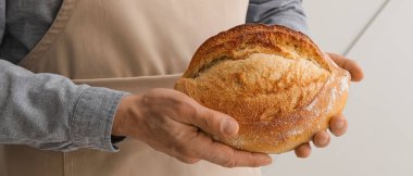 Hafif arka planda taze ekmeği olan erkek fırıncı, yakın plan.