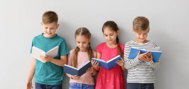 Cute little children reading books on grey background