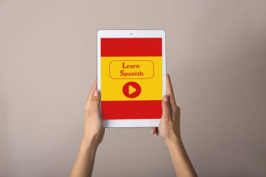 Ekranda gri arkaplana karşı Learn SPANISH yazılı tablet bilgisayarı tutan eller