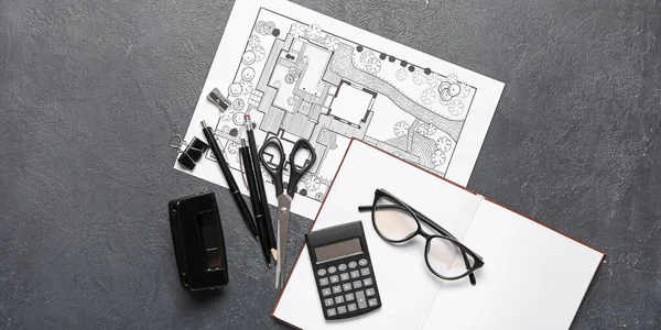 Landscape designer\'s plan with stationery, notebook and eyeglasses on dark background