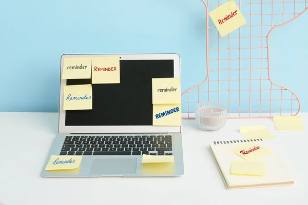 Laptop with sticky notes on table near blue wall