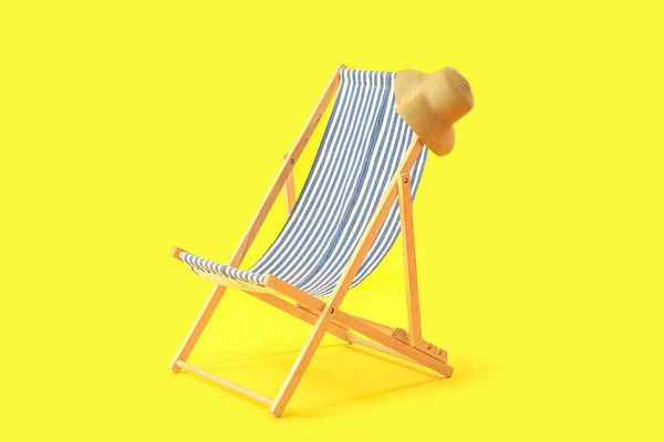 Wooden deck chair with hat on yellow background
