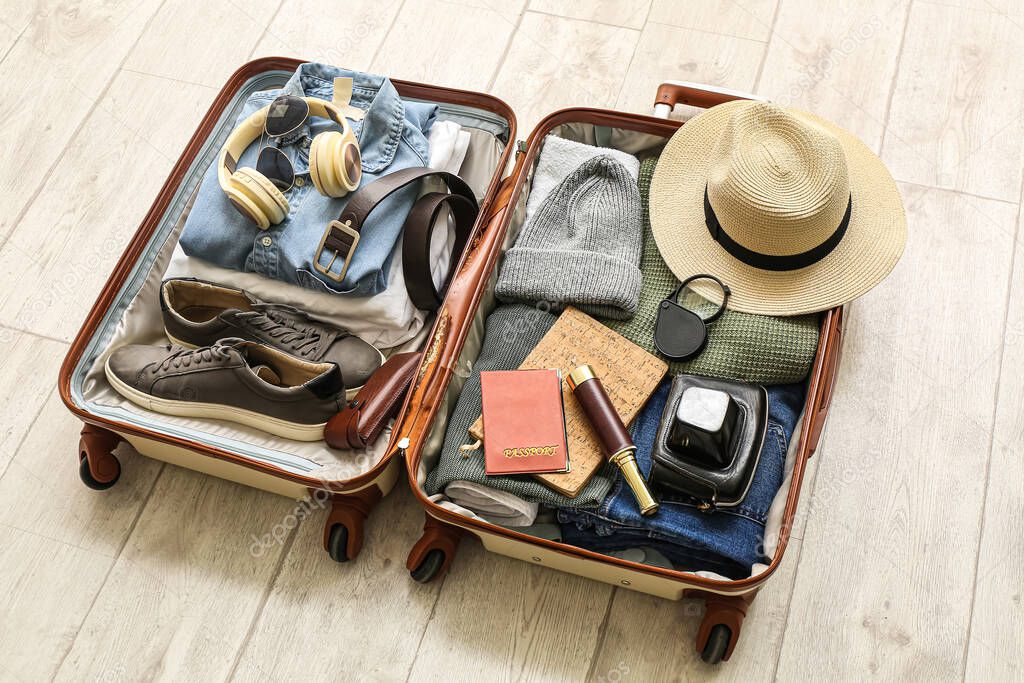 Suitcase with male accessories for travelling on white wooden background