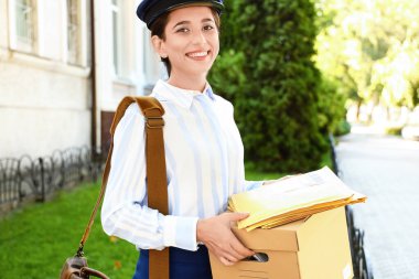 Young postwoman with box and letters outdoors