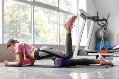 Genç bir kadın spor salonunda köpükle egzersiz yapıyor.