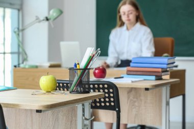 Sınıftaki masada kalem bardaklı ve gözlüklü elma.