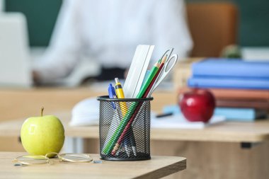 Sınıftaki masada kalem bardaklı ve gözlüklü elma, yakın plan.