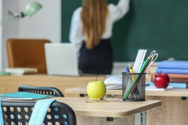 Apple with pen cup and eyeglasses on table in classroom