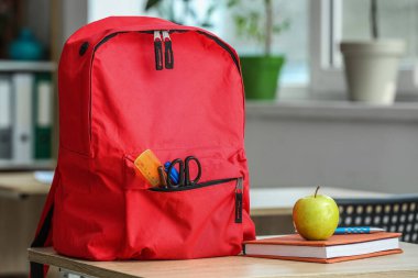 Apple with book and school backpack on table in classroom