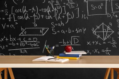 Elmalı kitap, kalem bardağı ve gözlüklü karatahtanın yanındaki masada.