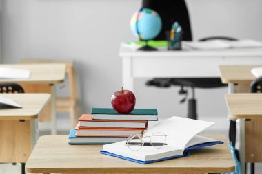 Red apple with school books and eyeglasses on table in classroom