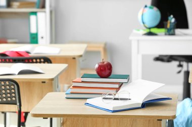 Red apple with school books and eyeglasses on table in classroom
