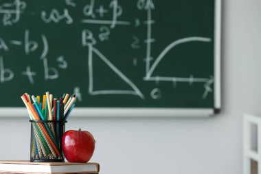 Okul kitaplarıyla kırmızı elma ve sınıfta kalem fincanı, yakın plan.