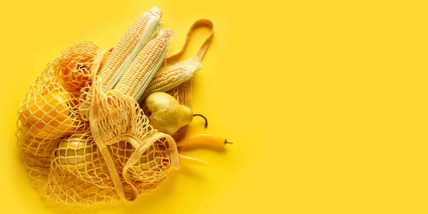 Mesh bag with fresh vegetables and fruits on yellow background with space for text