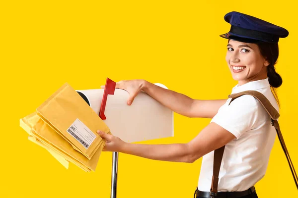 Young Postwoman Putting Letters Mailbox Yellow Background — Fotografia de Stock