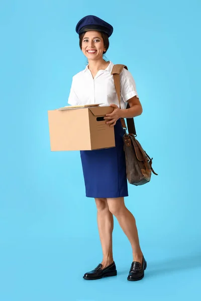 Young postwoman with box and bag on blue background